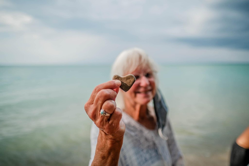 Heart-shaped stone held against a shoreline backdrop